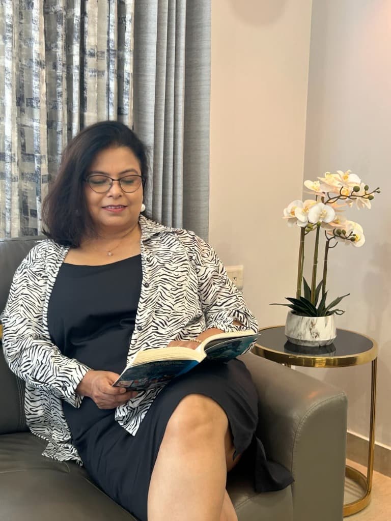 Vandana sitting on a couch reading a book in a peaceful environment